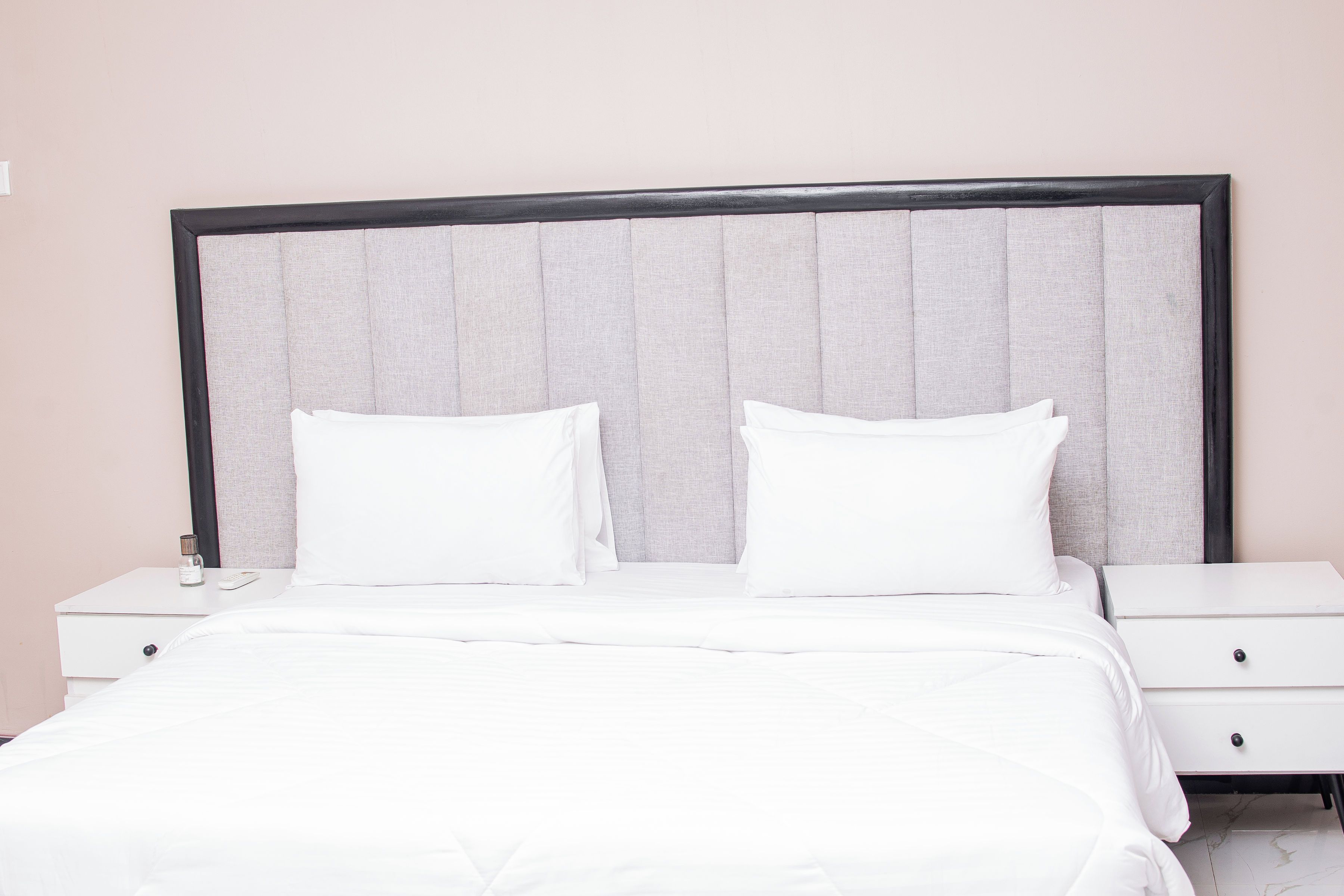 A neatly made bed with white bedding, a headboard with a grey upholstered panel, and two bedside tables with drawers.