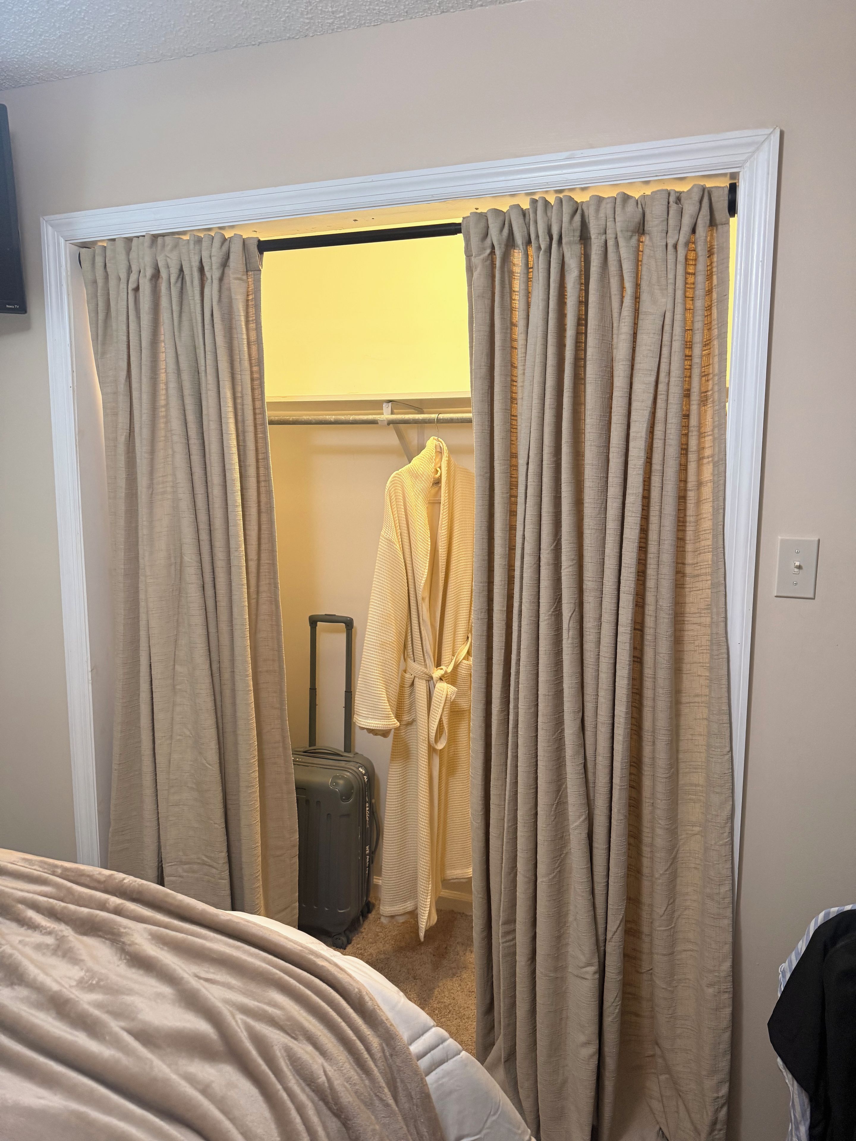 Quarto de hotel com cama, mala e roupão pendurado em um suporte.
