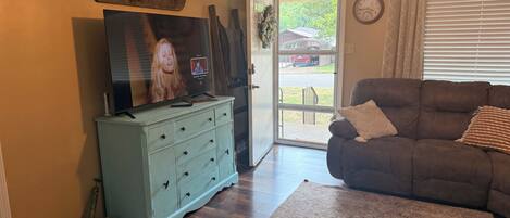 A living room with a television on a dresser, a couch, a rug, and a door leading outside.