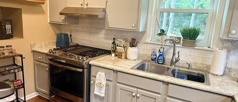 A kitchen with a stove, oven, sink, and window with a view of trees.