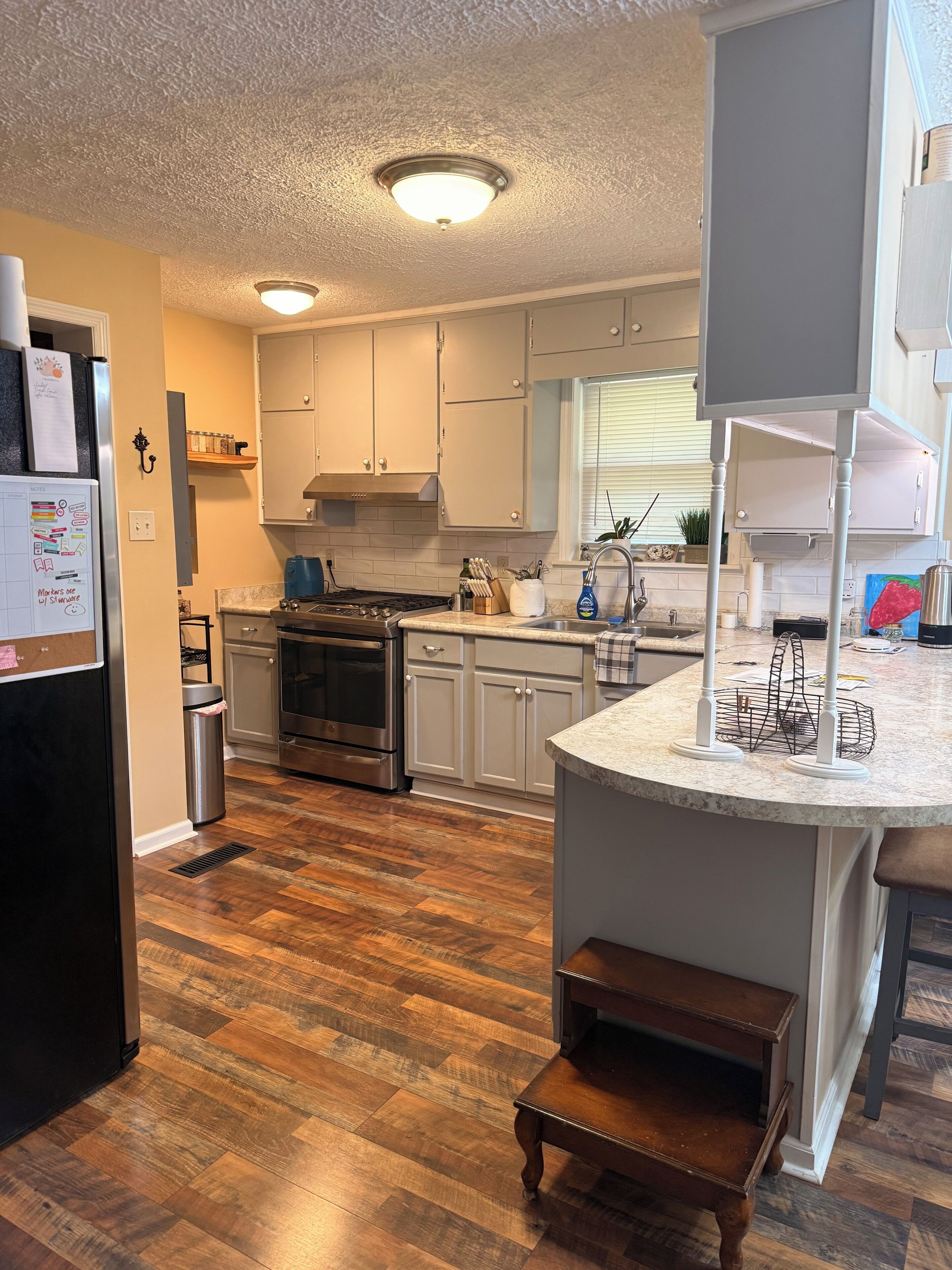 A kitchen with white cabinets, a stainless steel refrigerator, a built-in oven, and a wooden floor.