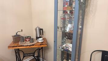 A room with a vintage Singer sewing machine, a wooden table, a tall cabinet with glass doors, and a hanging plant.