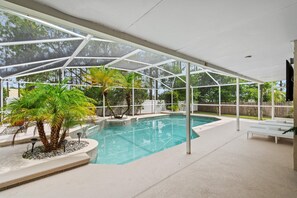 A covered swimming pool with a glass enclosure, palm trees, and a white fence in the background. - Highlands Reserve 101 (Orlando)