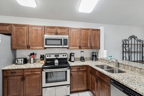 A kitchen with wooden cabinets, a stainless steel microwave, a gas stove, a coffee maker, and a dishwasher. - Highlands Reserve 101 (Orlando)