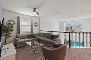 A spacious balcony with a pool, a gray sectional sofa, a glass coffee table, and a ceiling fan. - Storey Lake Resort 545 (Orlando)