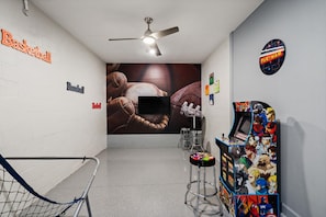 A hallway with a basketball and baseball sign, a ceiling fan, a TV screen, and a Pac-Man arcade machine. - Storey Lake Resort 545 (Orlando)