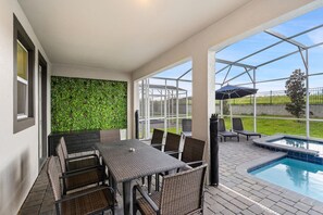 A covered patio area with a pool, outdoor seating, and a view of the surrounding landscape. - Championsgate 897 - Ten Bedroom Villa, Sleeps 33 (Orlando)