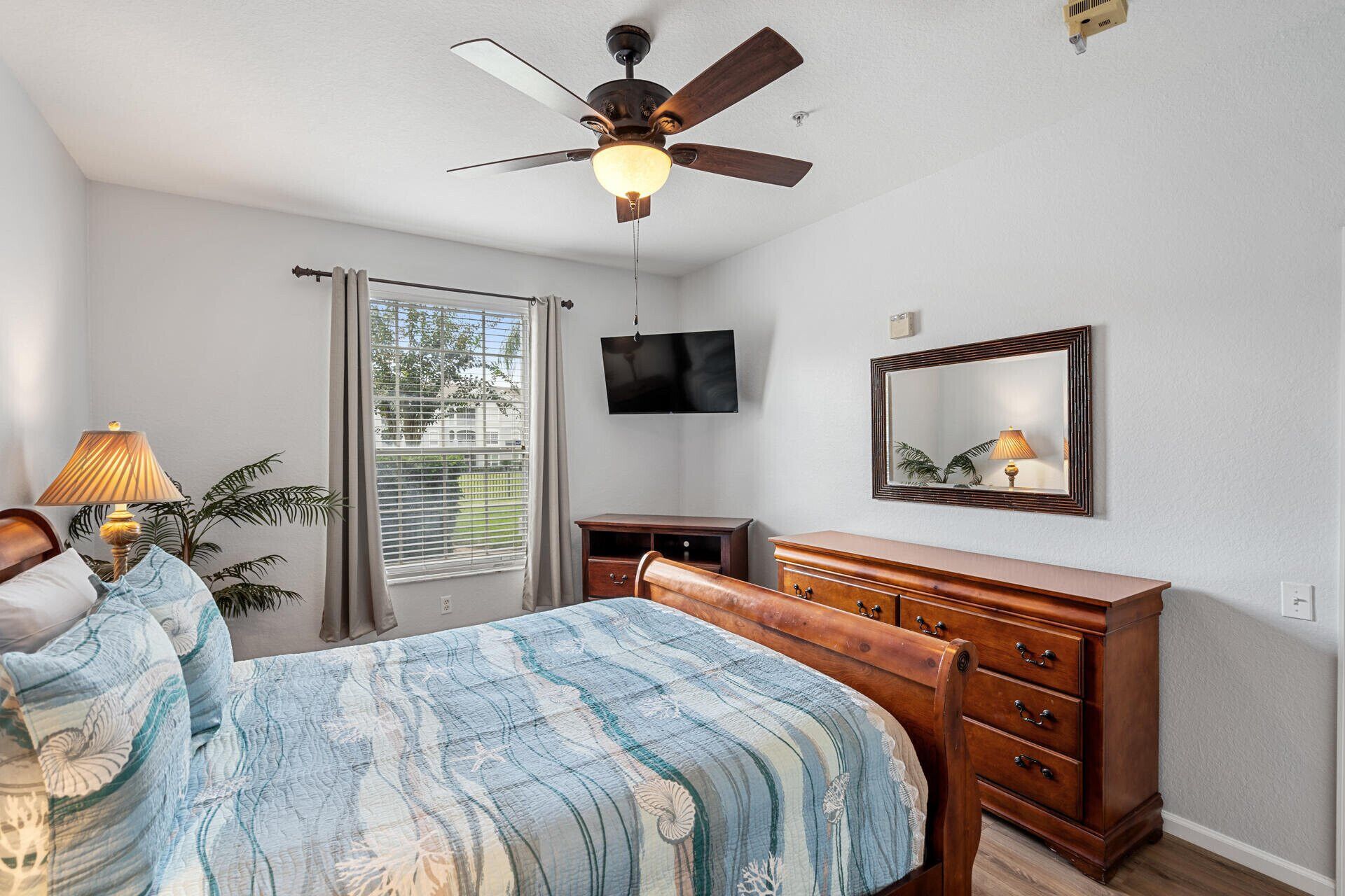 A bedroom with a bed, a dresser, a ceiling fan, a TV, and a window with blinds.