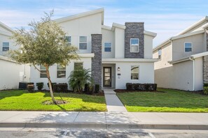 A modern two-story residential building with a stone accent wall, a front door, and a well-maintained lawn. - Championsgate 923 - Eight Bedroom Villa, Sleeps 20 (Orlando)