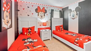 Una stanza con due letti, ognuno con copriletto a tema Topolino, un muro con carta da parati di Topolino e una ventola a soffitto.