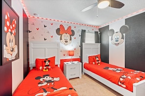 A room with two beds, each with a Mickey Mouse-themed bedspread, a wall with Mickey Mouse wallpaper, and a ceiling fan. - Windsor Island Resort 463 (Orlando)