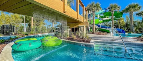A pool area with a wooden deck, a water slide, and inflatable rings.