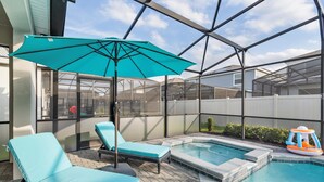 Un giardino sul retro con piscina, due poltrone relax, un ombrellone blu e una piccola piscina gonfiabile.