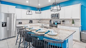 Una cucina moderna con mobili bianchi, un'isola centrale con sgabelli da bar, elettrodomestici in acciaio inossidabile e pareti di accent blu.