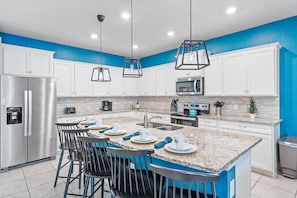 A modern kitchen with white cabinets, a central island with bar stools, stainless steel appliances, and blue accent walls. - Windsor Island Resort 463 (Orlando)