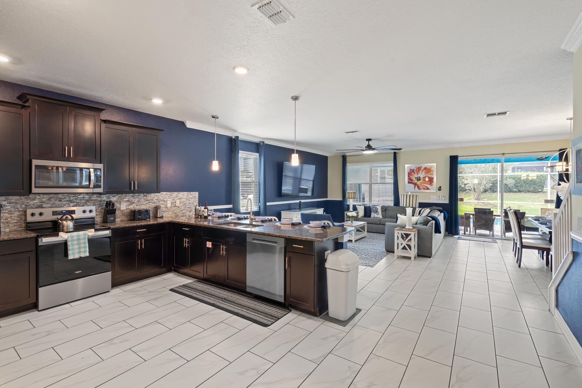 A modern kitchen with dark cabinetry, a central island, and a dining area with a view.