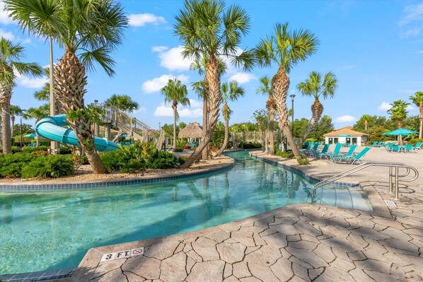 A pool area with clear water, palm trees, lounge chairs, and a water slide. - Championsgate 931 - Eight Bedroom Villa, Sleeps 20 (Orlando)