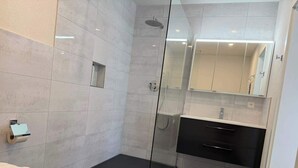 A modern bathroom with a glass shower enclosure, a toilet, a sink with a mirror, and a black vanity.