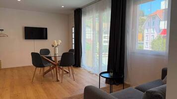 Une chambre moderne équipée d’une table à manger, de chaises, d’un téléviseur et d’une grande fenêtre avec des rideaux.