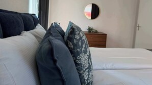 A neatly made bed with white linens and several pillows, including a floral one.