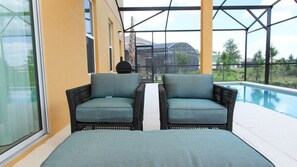 Zona de piscina con dos sillas de mimbre y un porche con paredes de vidrio.