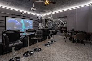 Un salón moderno con pantalla de proyector, asientos cómodos y un mural único.