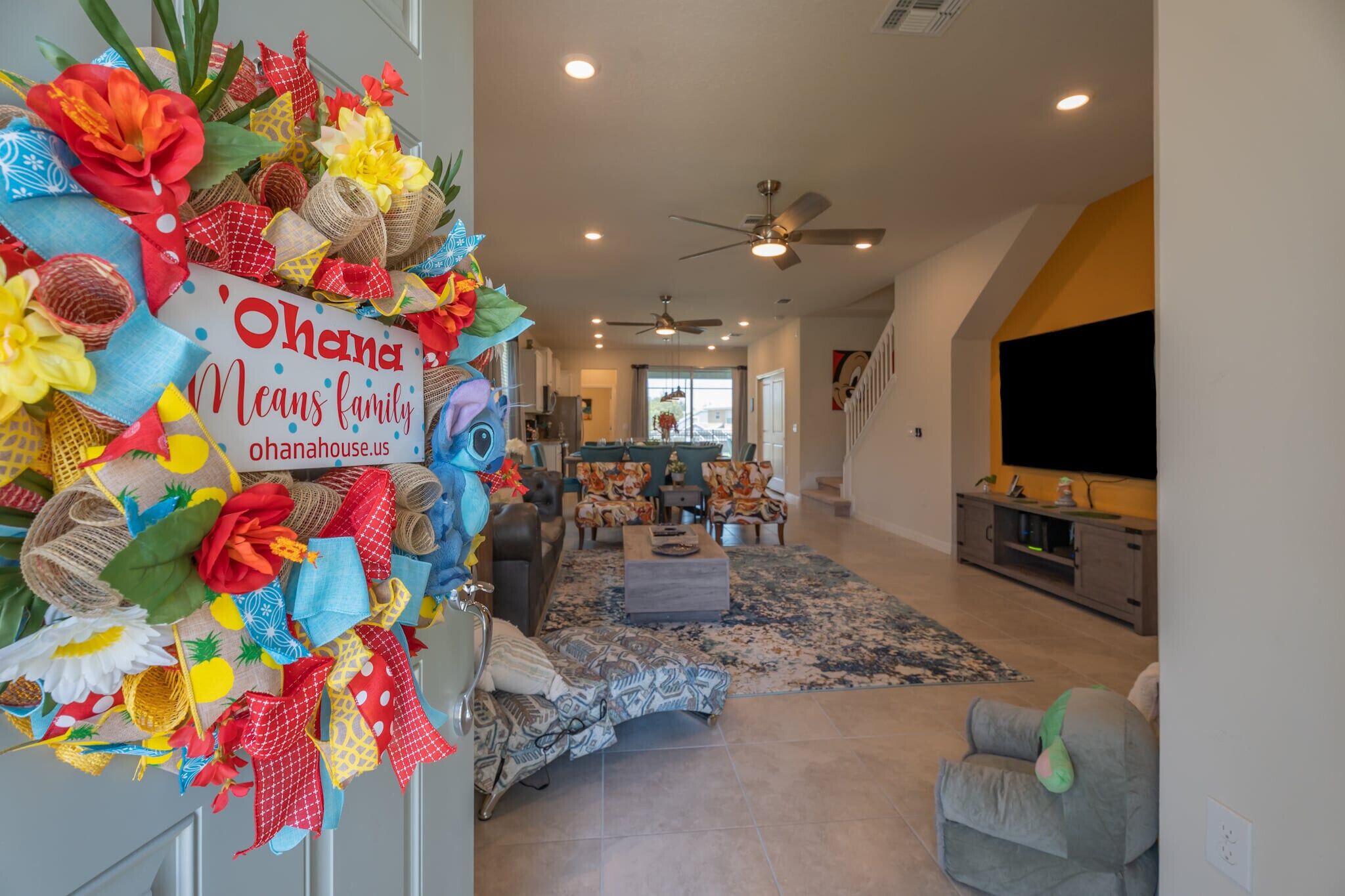 A spacious living room with a large TV, comfortable seating, and a decorative wreath on the door.