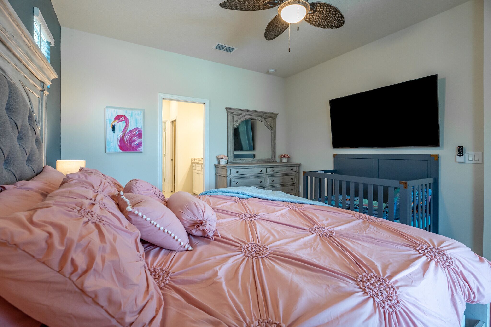Een slaapkamer met een groot bed, een dressoir, een televisie en een plafondventilator.