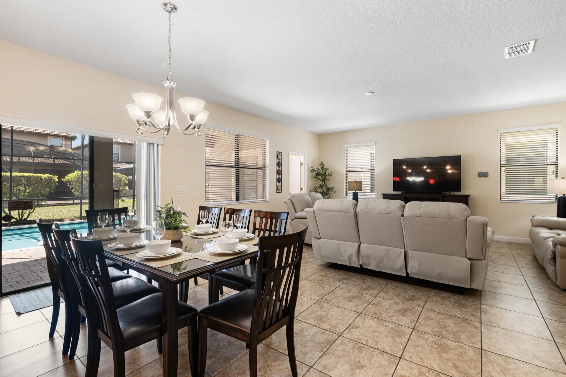 A dining area with a table set for four, a sofa, a TV, and a pool view.