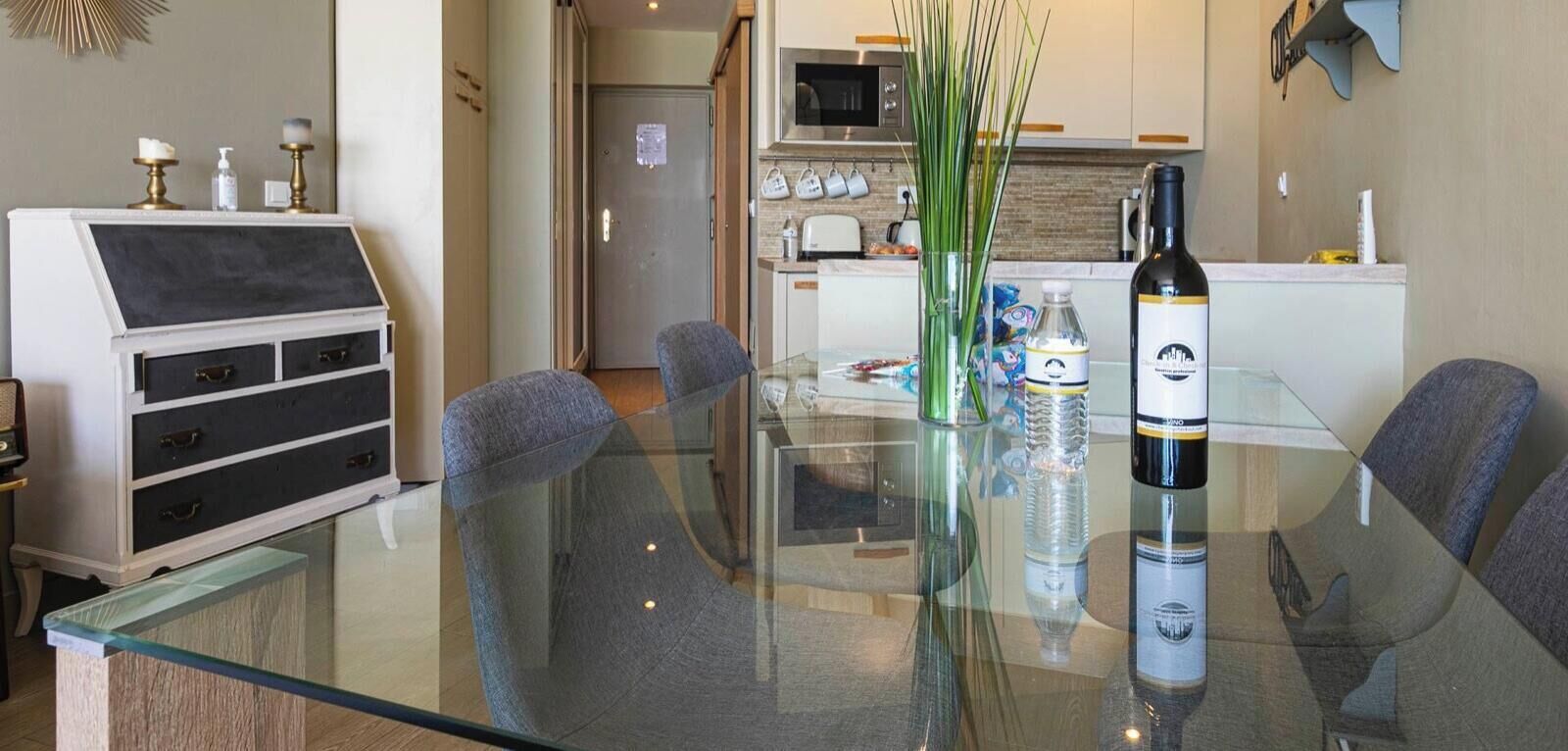 Una cocina moderna con una mesa de vidrio, sillas y una botella de vino.