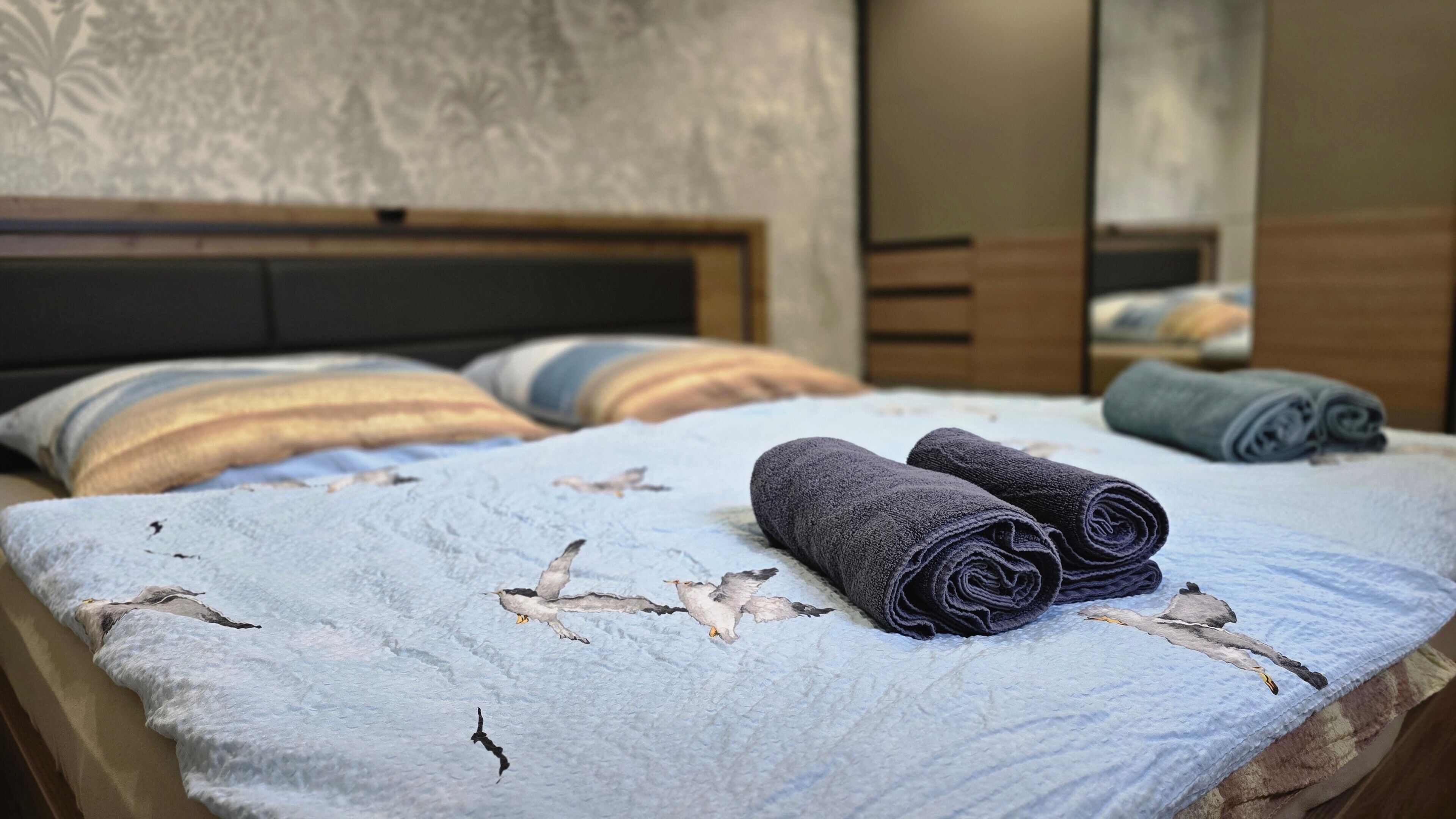 Un lit avec une couvre-lit à motifs, deux serviettes enroulées et des oreillers à rayures.