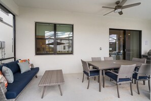 Een terras met een eettafel, stoelen, een bank en een plafondventilator.