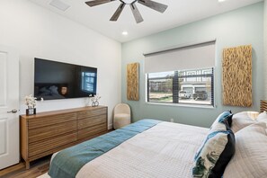 Ein Schlafzimmer mit einem Bett, einem an der Wand montierten Fernseher, einem Fenster mit Jalousien und einem Deckenventilator.
