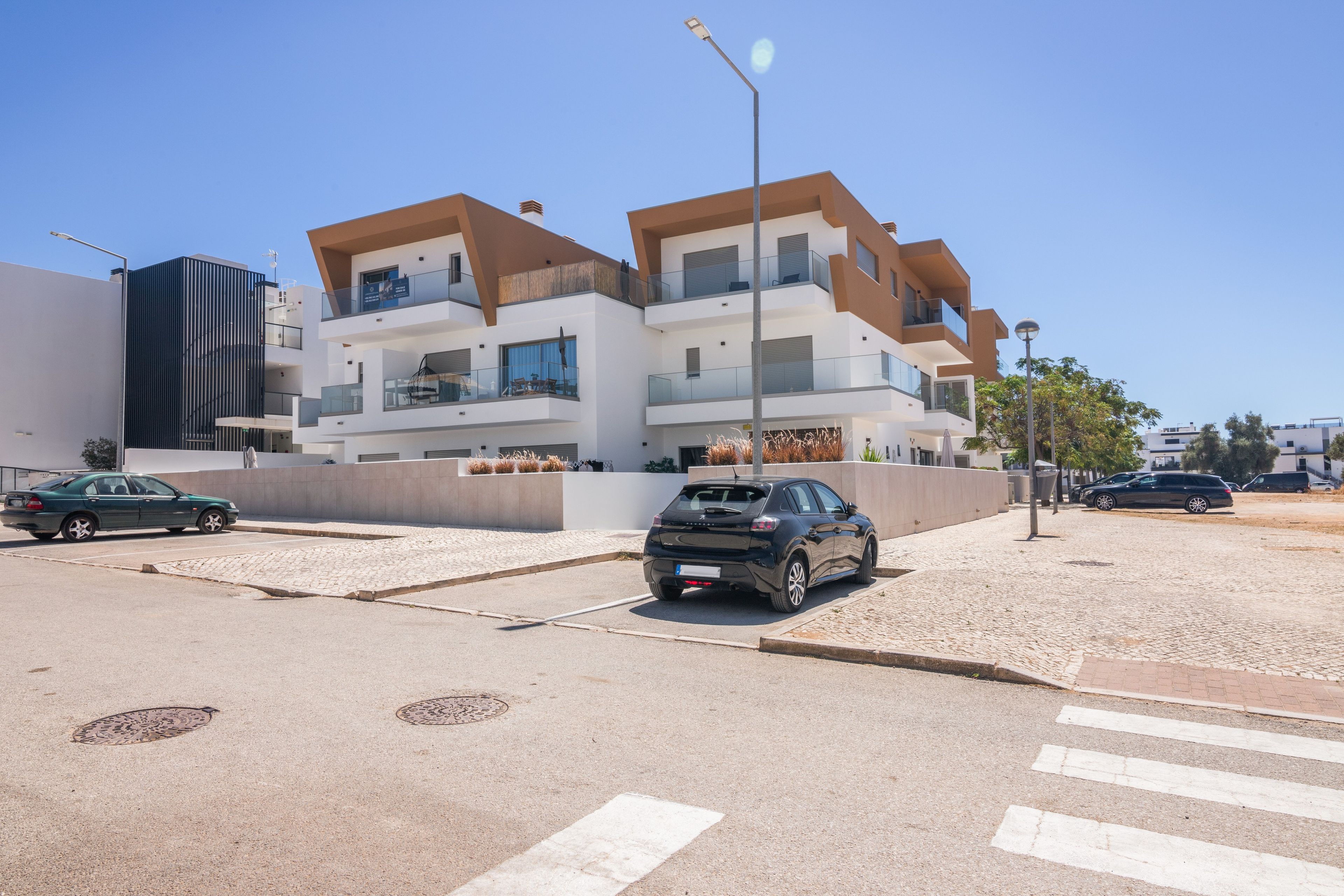 A modern multi-story residential building with balconies, a paved street, and parked cars.