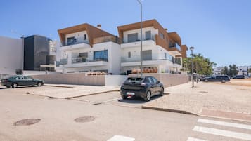 A modern multi-story residential building with balconies, a paved street, and parked cars.