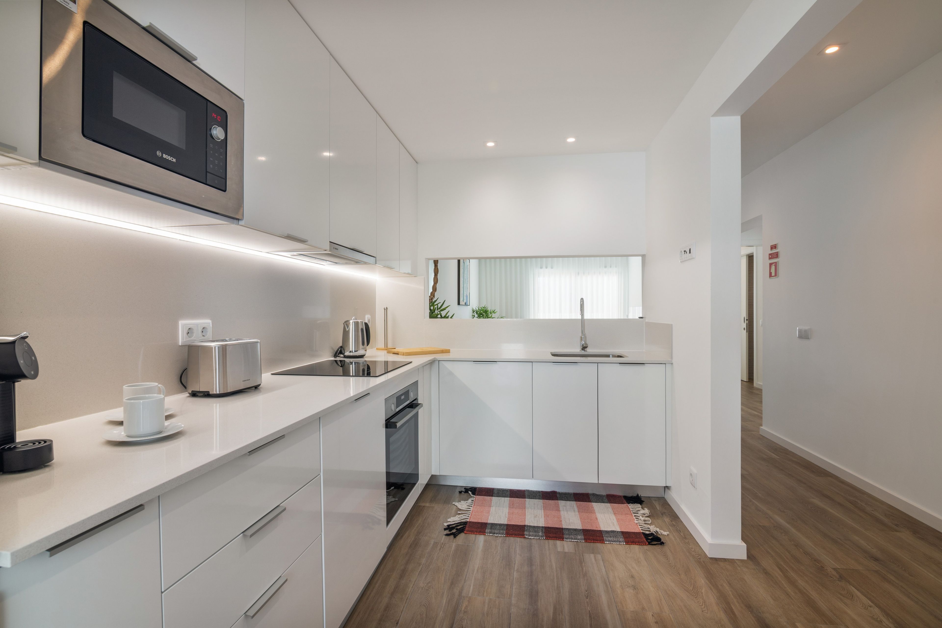Een moderne keuken met witte kasten, een ingebouwde magnetron, een broodrooster en een koffieapparaat.