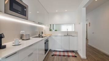 A modern kitchen with white cabinetry, a built-in microwave, a toaster, and a coffee machine.