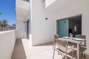 A balcony with a table set for dining, chairs, and a sliding glass door leading to an interior space. - Apartment Luxury 2br with Terrace  5-min Walk beach front (Tavira)