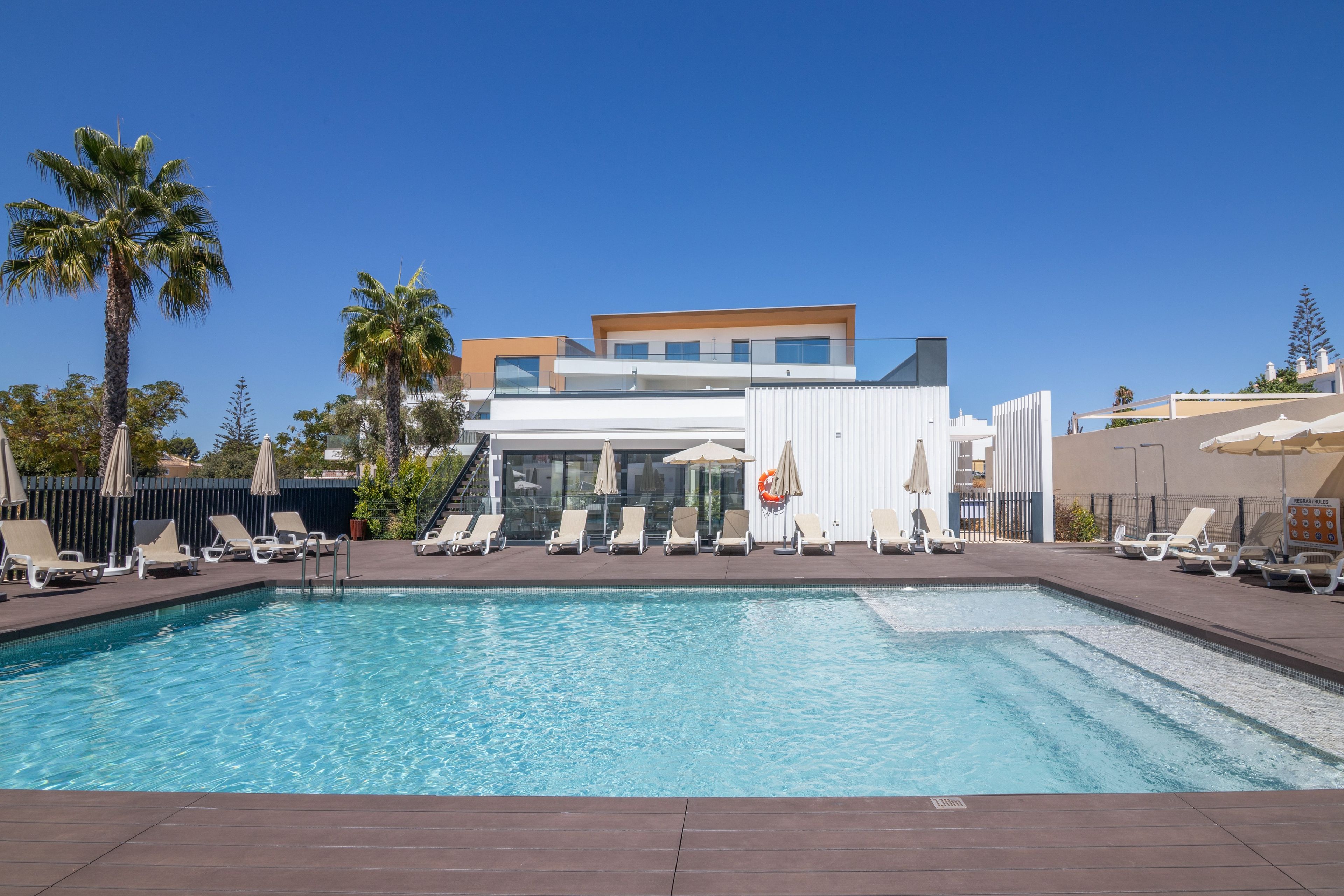Un hôtel moderne doté d’une piscine, de chaises longues et de palmiers.