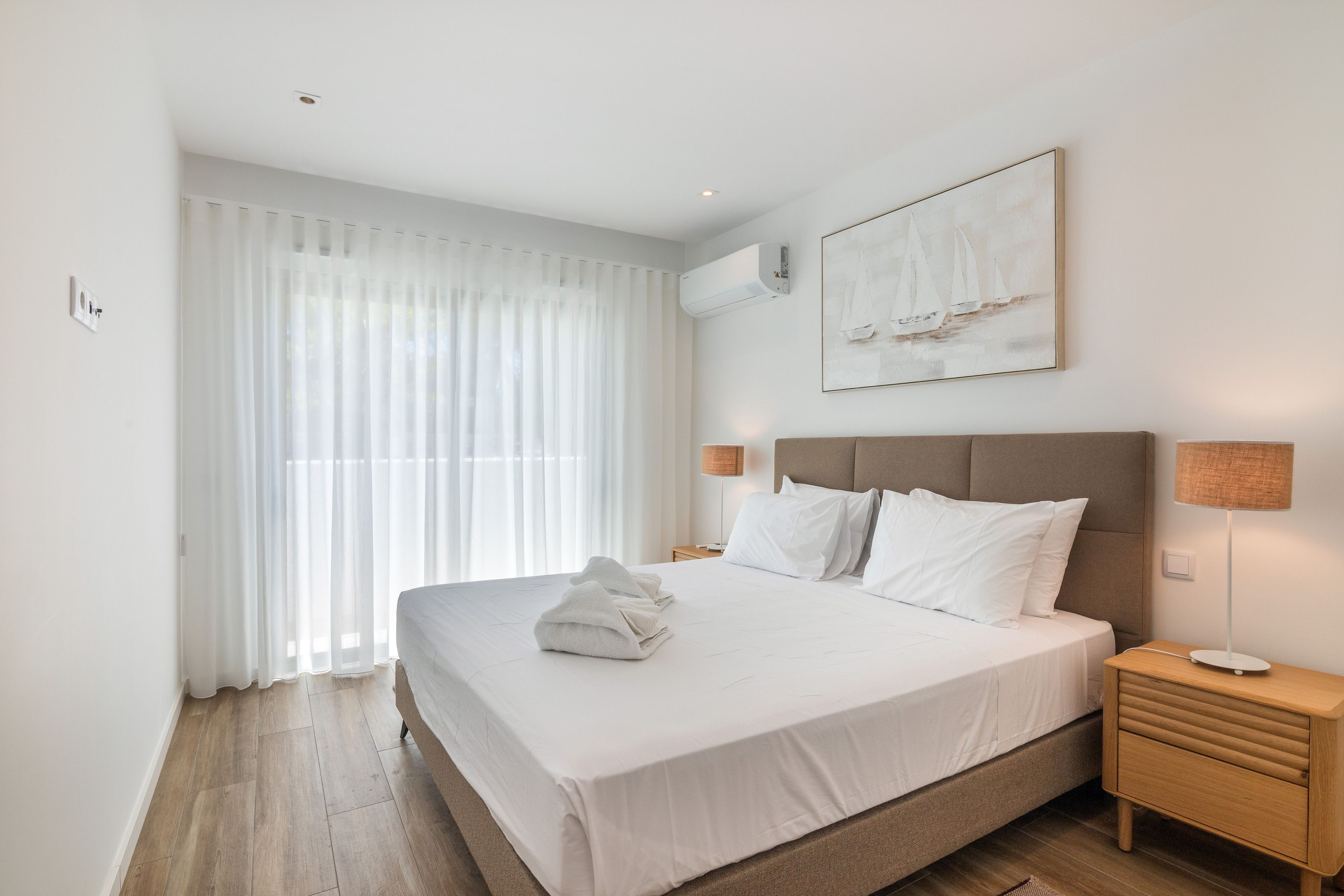 A hotel room with a large bed, a nightstand, a lamp, and a painting on the wall.
