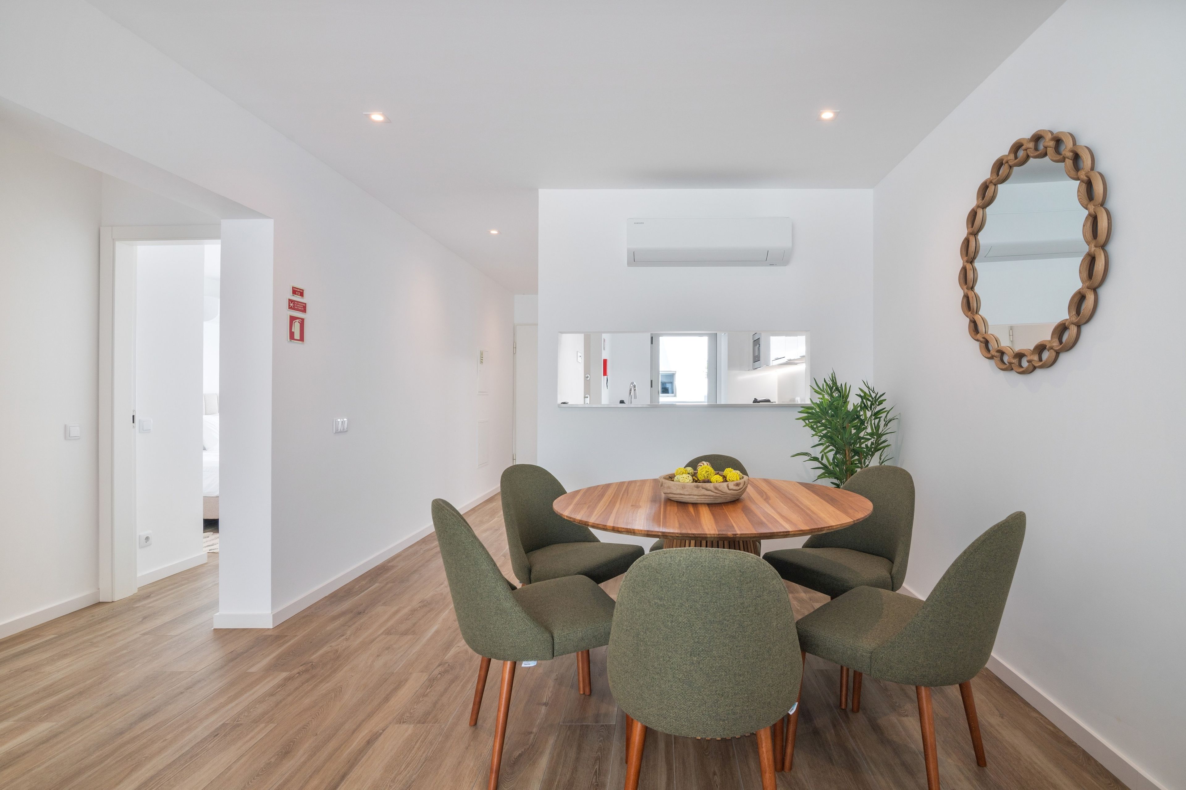 Un comedor moderno con una mesa redonda de madera, seis sillas tapizadas en verde y un espejo decorativo en la pared.