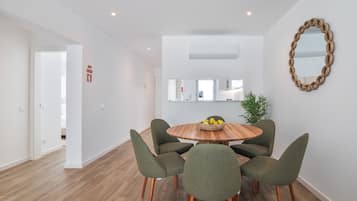 A modern dining area with a round wooden table, six green upholstered chairs, and a decorative mirror on the wall.