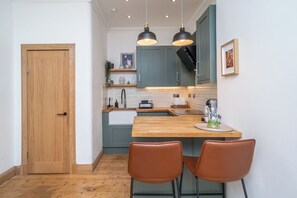 A compact kitchen with a wooden door, two pendant lights, a sink, and a small island with chairs. - Quiet Beach Retreat | Free Parking - Pass the Keys (Edinburgh)