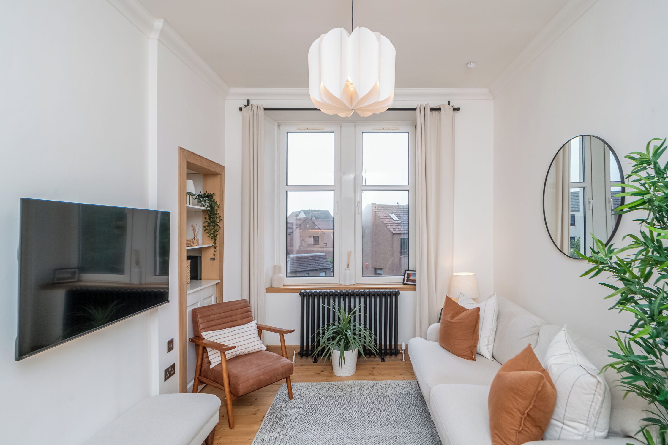 Un salon moderne avec un téléviseur à écran plat, un canapé, un fauteuil, une plante en pot et une grande fenêtre avec des rideaux.