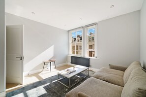 A modern living room with a sofa, coffee table, and a view of the city through large windows. - Cosy and Stylish Flat in Notting Hill - Pass the Keys (London)