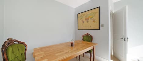 Un coin repas avec une table en bois, deux chaises rembourrées, une carte du monde accrochée au mur et une porte donnant sur une autre pièce.