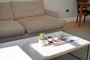 Een woonkamer met een bank, een salontafel met een tijdschrift en een kleine plant.