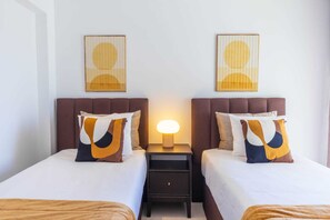 Ein Hotelzimmer mit zwei Betten, einem Nachttisch mit Lampe und zwei an der Wand befestigten Kunstwerken.