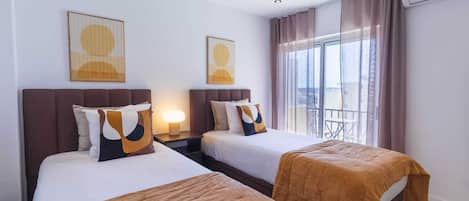 A hotel room with two beds, a nightstand with a lamp, and a balcony with a view.