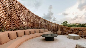 An outdoor seating area with a curved sofa, a round table, and two woven poufs. - Aflora Moon 3 bd First FloorBeach Club + Breakfast (Tulum)